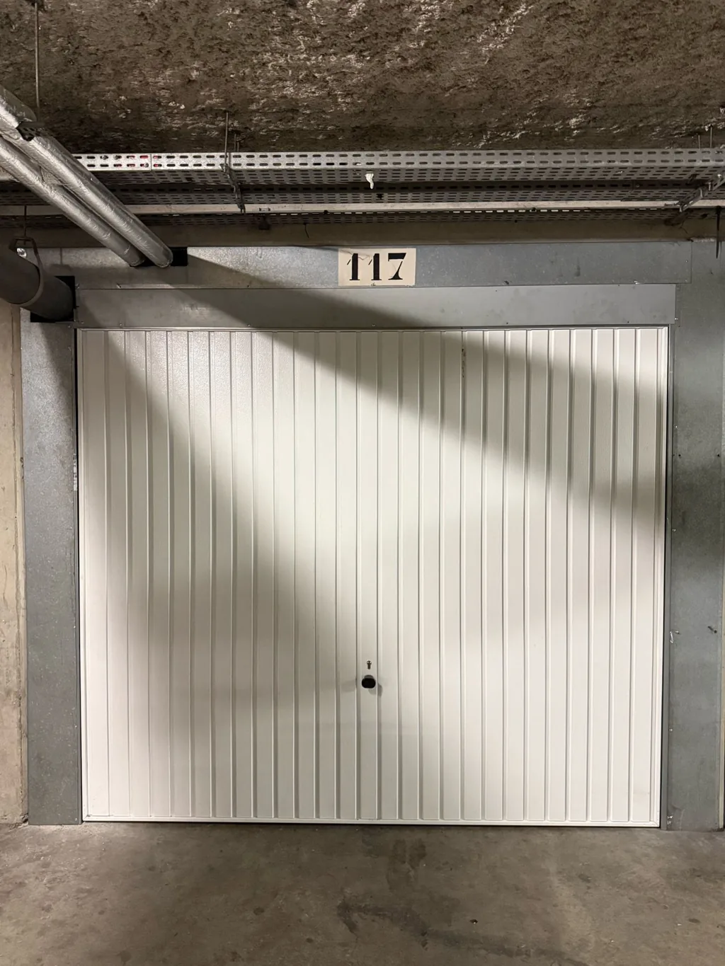 Porte basculante blanche neuve posée dans un box en sous-sol