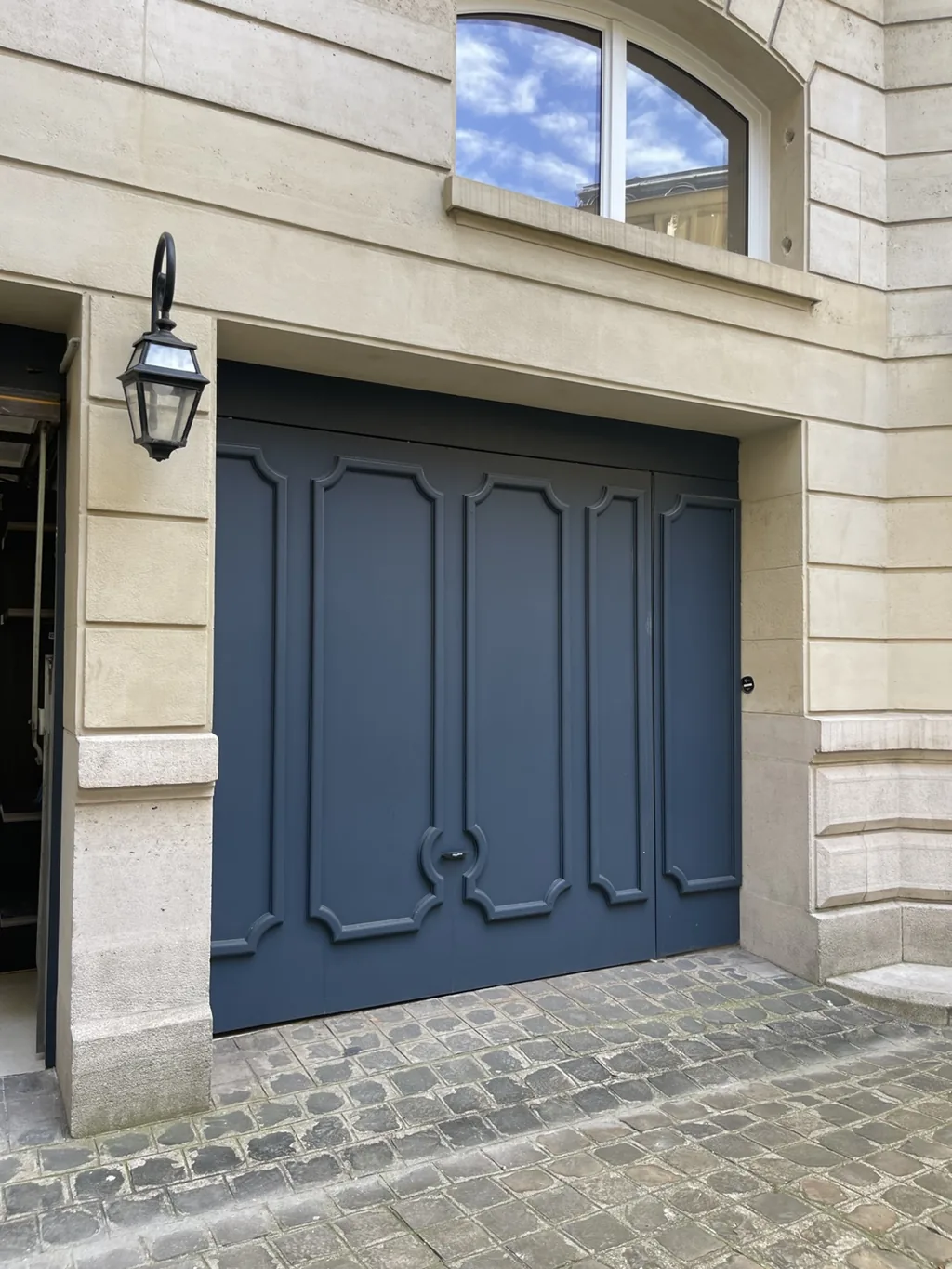 Porte de garage battante bleu nuit à panneaux moulurés dans une façade en pierre de taille