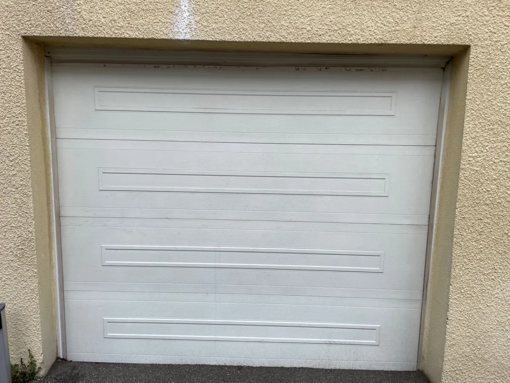 Porte de garage sectionnelle blanche à moulures posée sur un pavillon