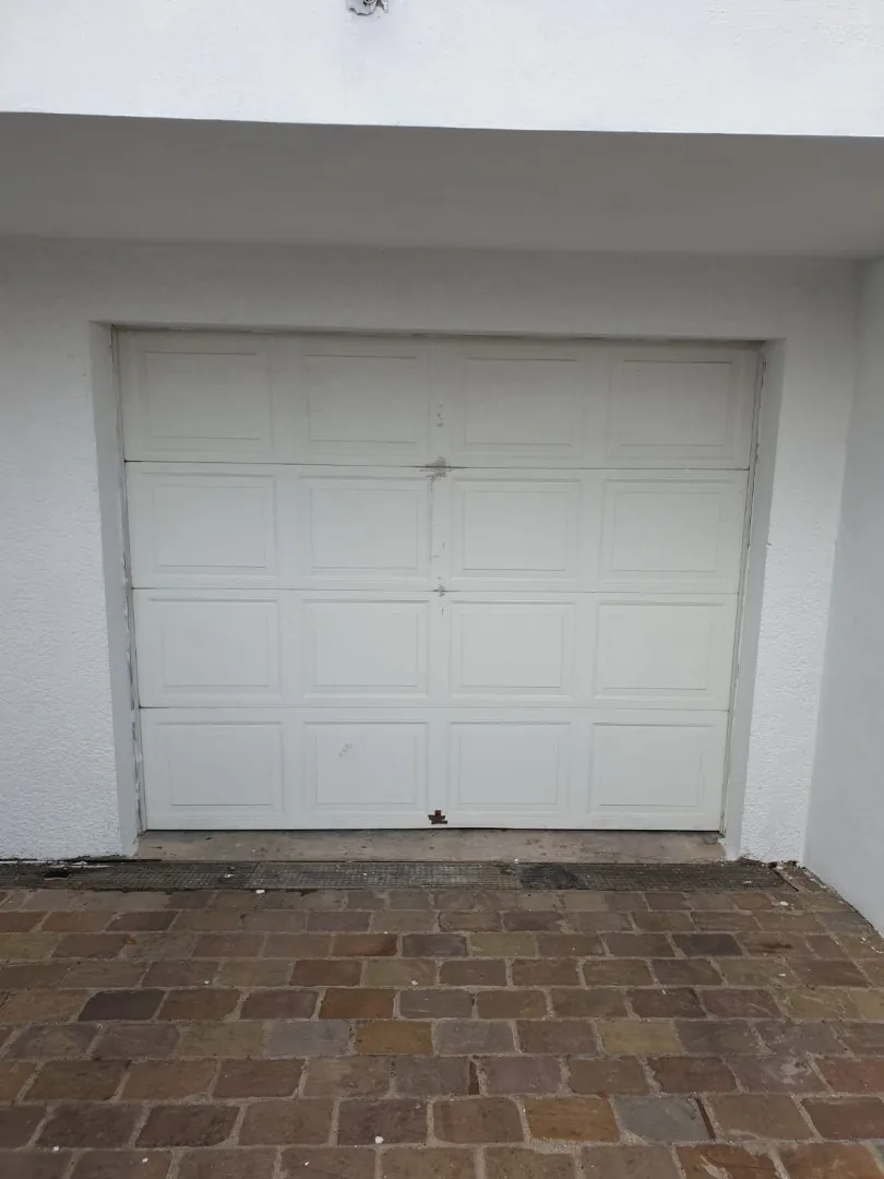 Porte de garage sectionnelle blanche à cassettes posée sur une façade en crépi