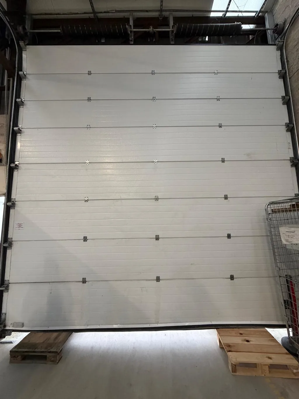 Porte sectionnelle industrielle pleine hauteur installée dans un entrepôt, ressorts de torsion visibles